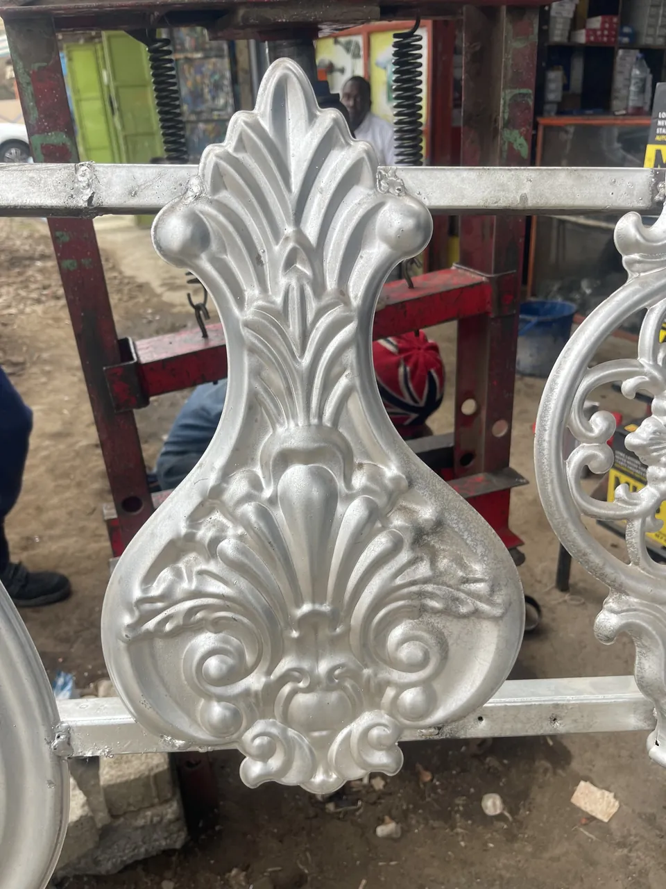 Silver-colour gate flower with tall leaf forms and scrollwork photographed on a rail