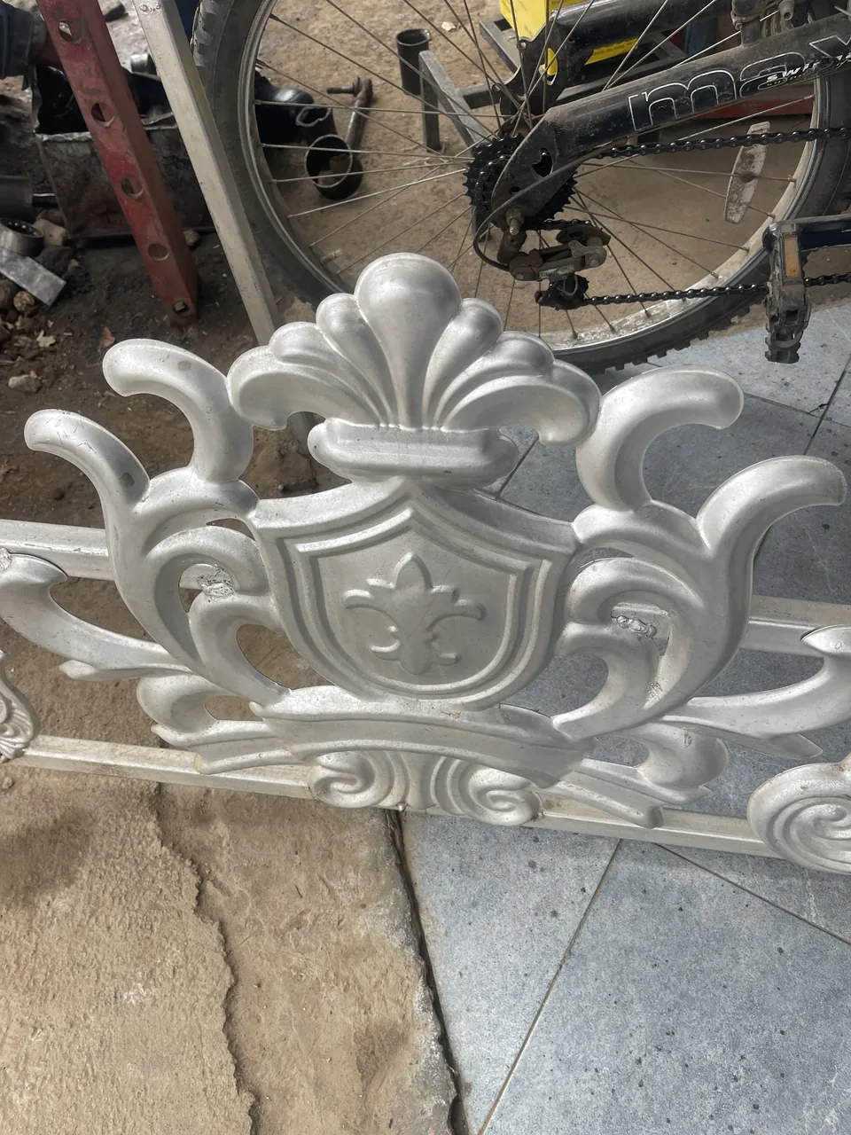 Silver-colour crown and shield gate flower with scrollwork photographed on a gate rail